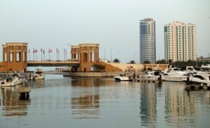 A modern marina with yachts, bridge, and waterfront city skyline reflecting on calm waters.