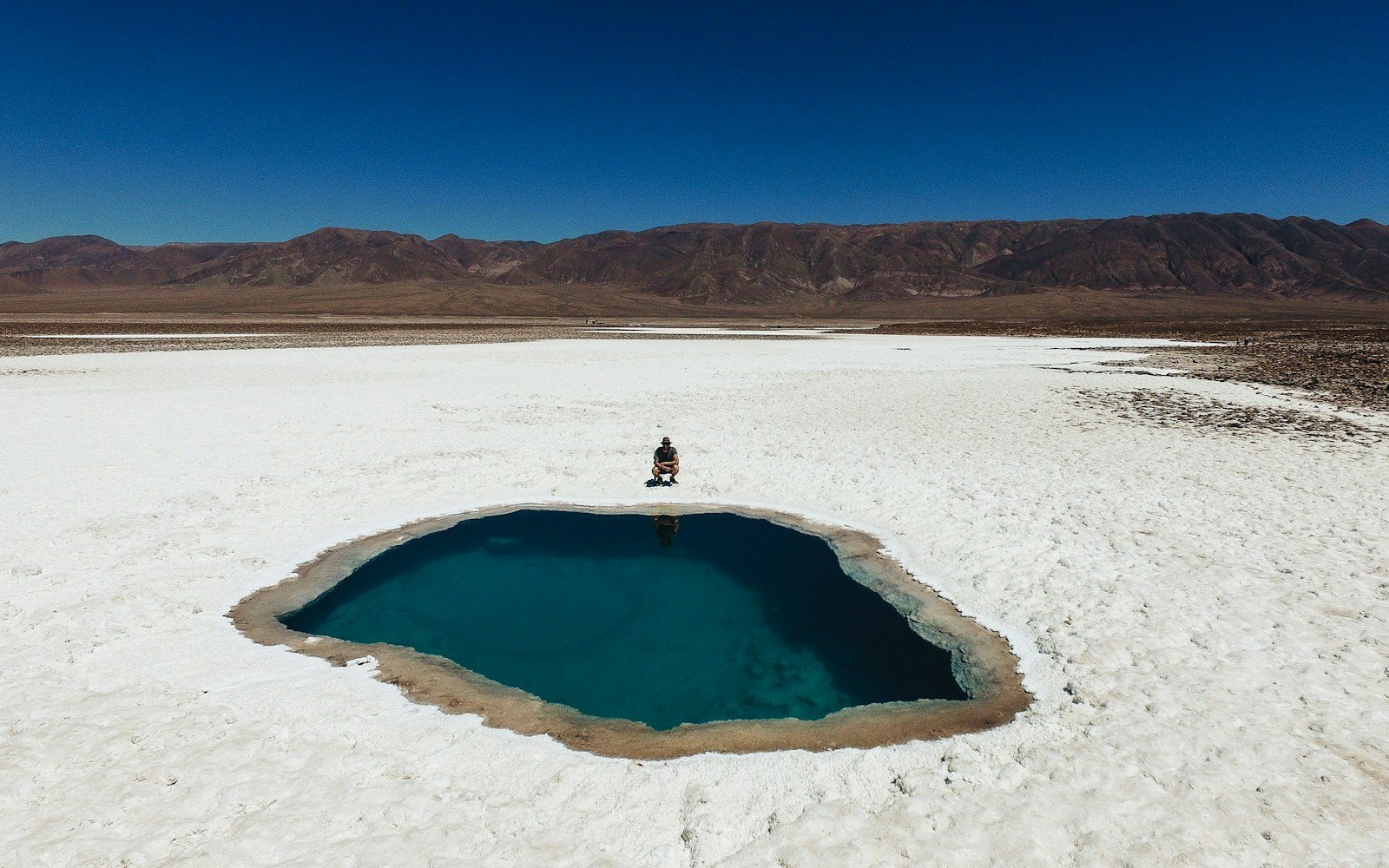 person wearing black shirt sitting near blue hole under blue sky during daytime