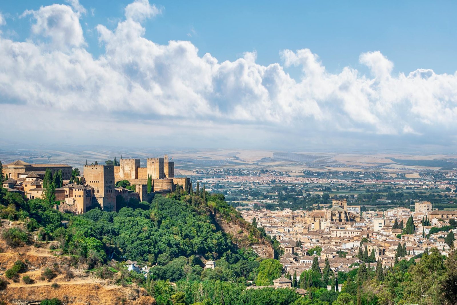 A scenic view of the historic Alhambra in Granada, Spain, surrounded by lush greenery and an expansive cityscape.