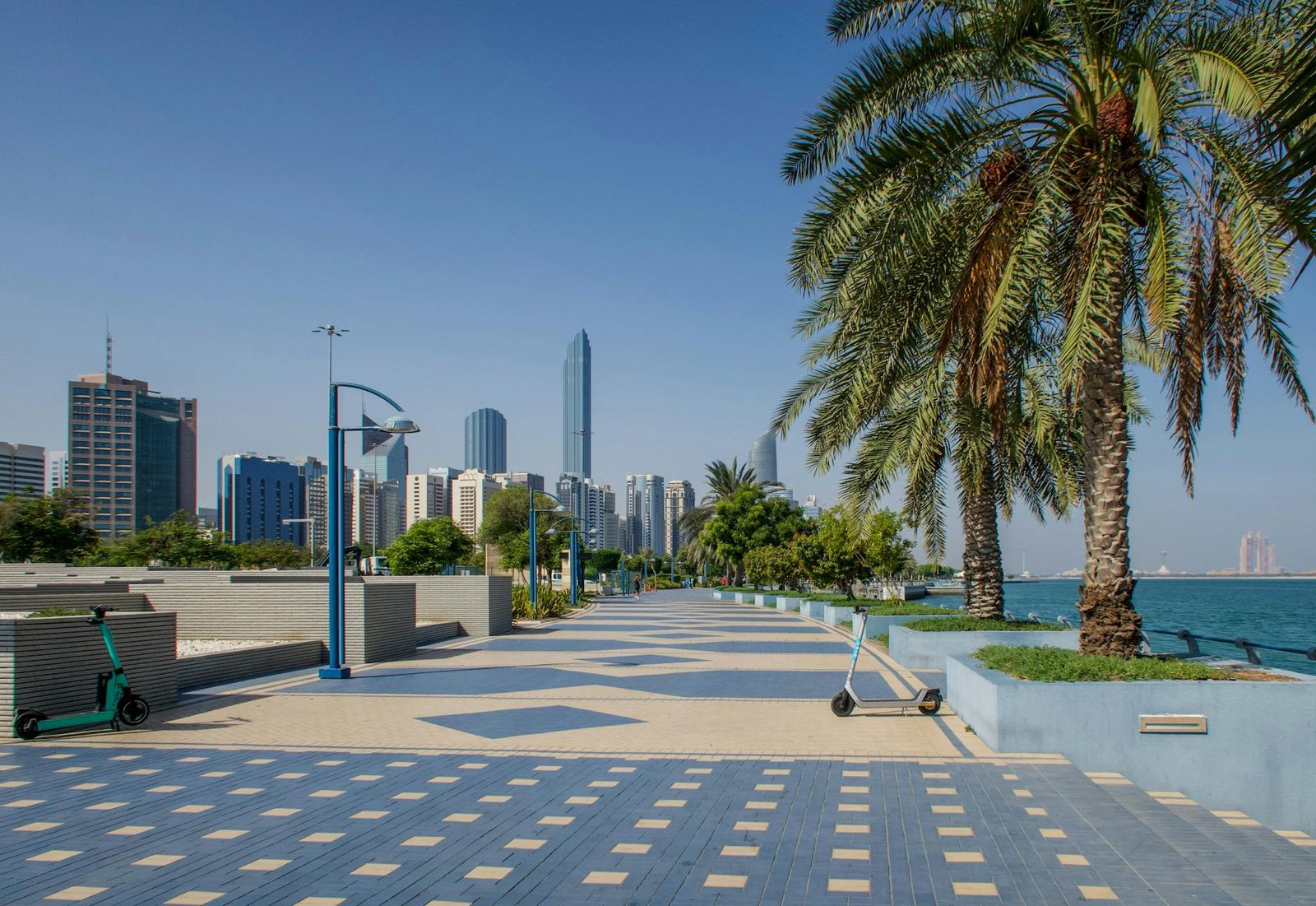 Vibrant view of Abu Dhabi skyline from Corniche with palm trees and sea.
