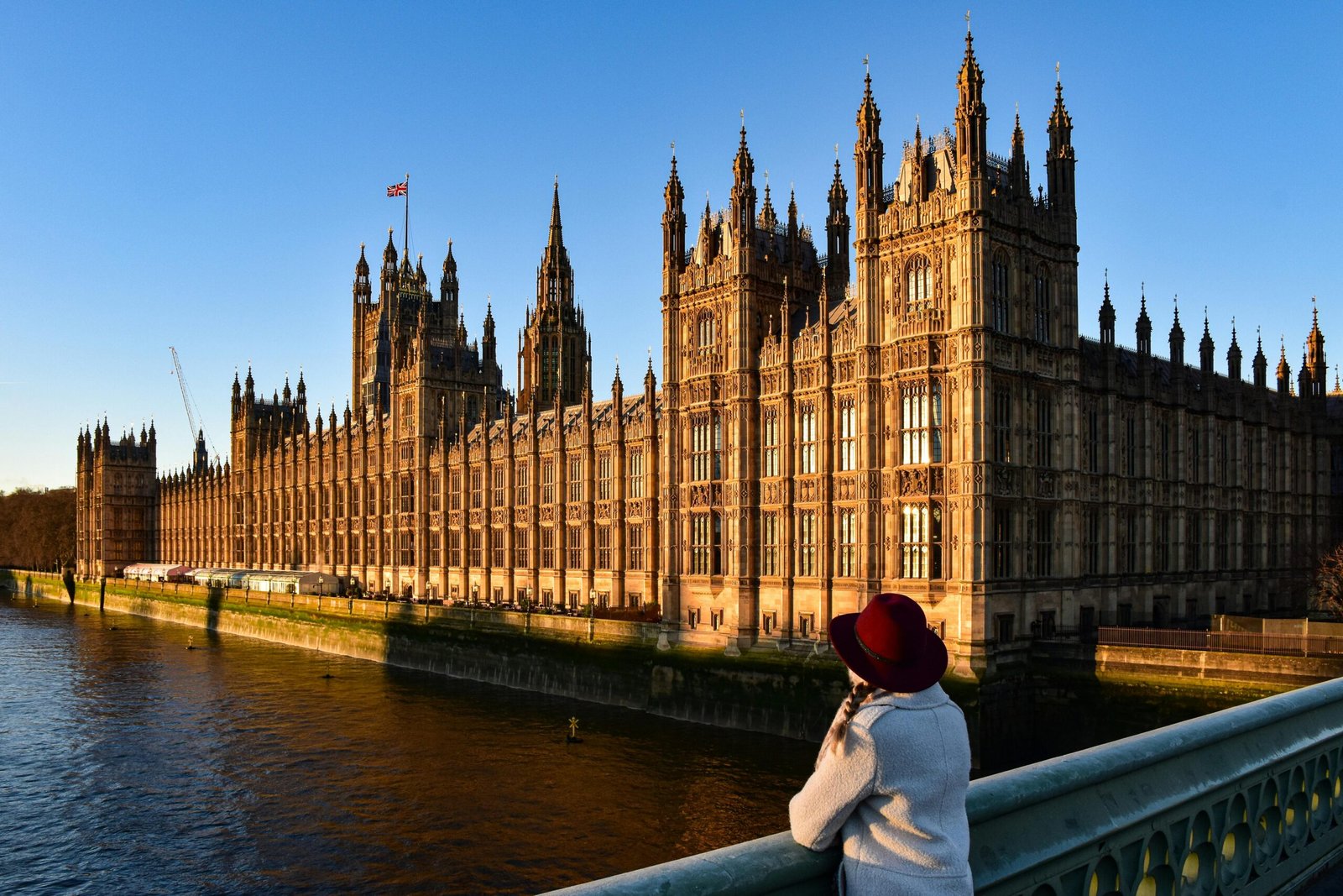 Photograph of Westminster Palace with a person enjoying the view from Westminster Bridge at sunset.